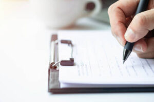 Close-up of Hand using writing pen with questionnaire or paperwork survey question filling in business company personal information form checklist document.